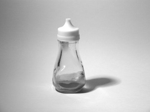 A glass and plastic salt shaker containing a grey powder